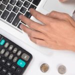 calculadora y mano escribiendo en un ordenador